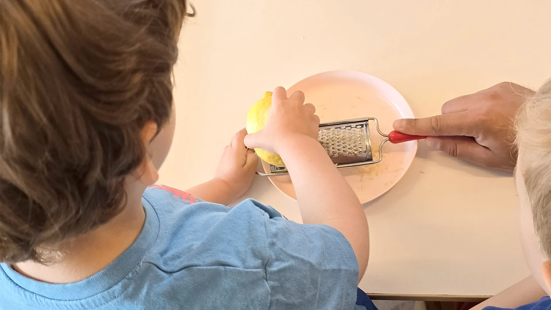 Gros plan sur des petites mains râpant un citron avec enthousiasme pendant l’activité culinaire.