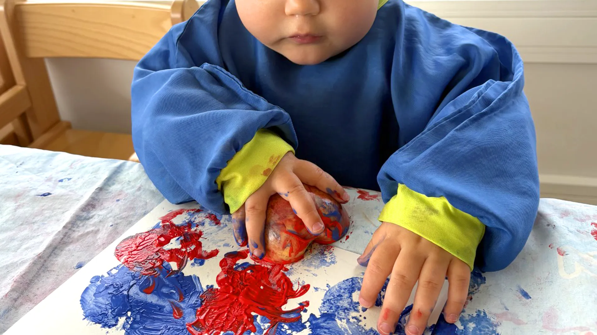 enfant tenant une pomme colorée couverte de peinture, à la crèche Les 6 Sens à Saint-Sulpice.