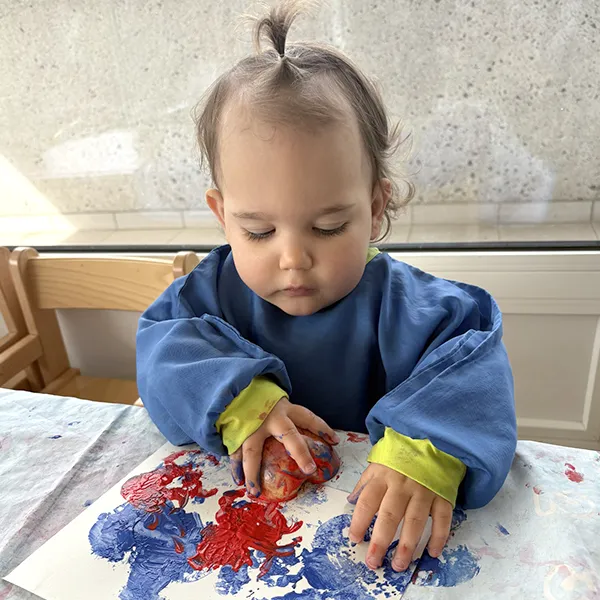 enfant tenant une pomme colorée couverte de peinture, à la crèche Les 6 Sens à Saint-Sulpice.