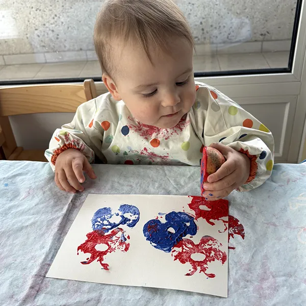 enfant tenant une pomme colorée couverte de peinture, à la crèche Les 6 Sens à Saint-Sulpice.