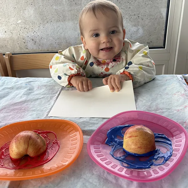 enfant tenant une pomme colorée couverte de peinture, à la crèche Les 6 Sens à Saint-Sulpice.