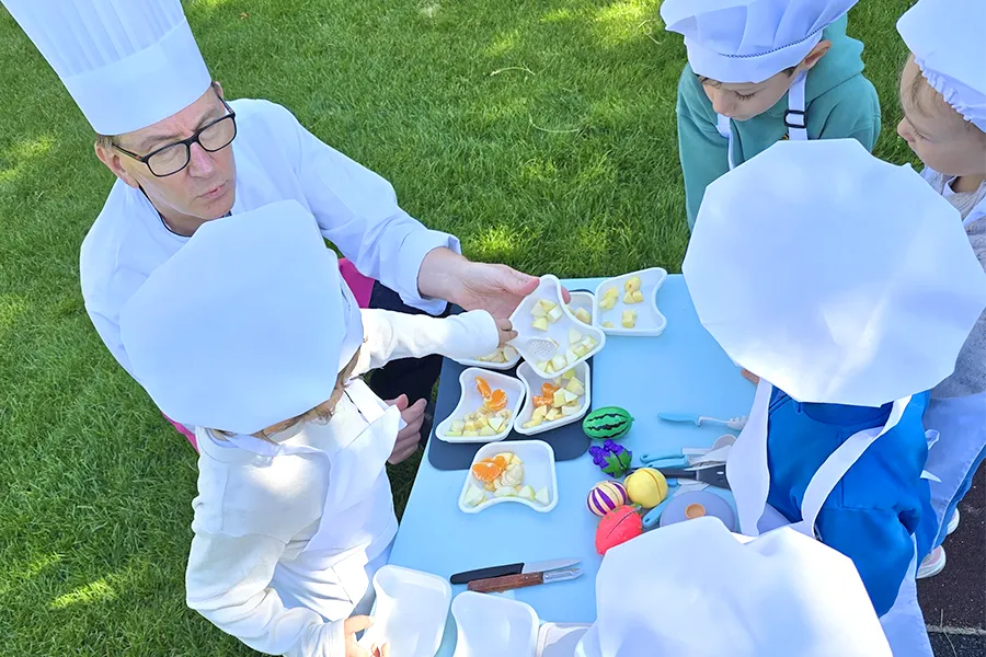 Enfants du groupe des Grands en pleine préparation de leur salade de fruits à la crèche 6 Sens, encadrés par un professionnel de Novae à Saint-Sulpice.