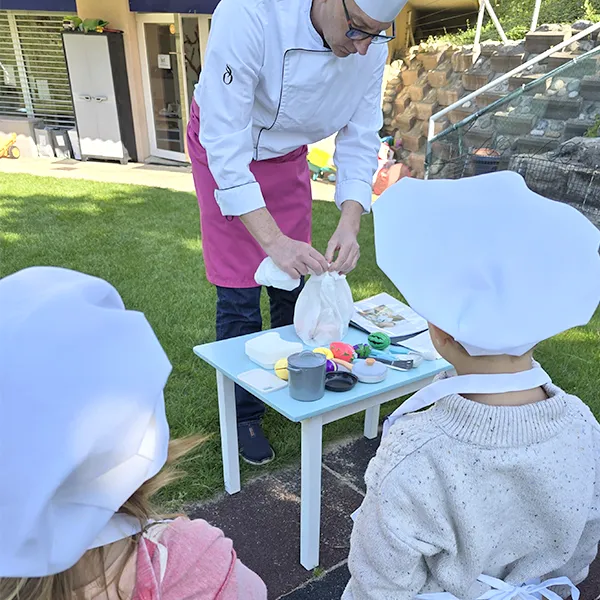 Enfants du groupe des Grands en pleine préparation de leur salade de fruits à la crèche 6 Sens, encadrés par un professionnel de Novae à Saint-Sulpice.