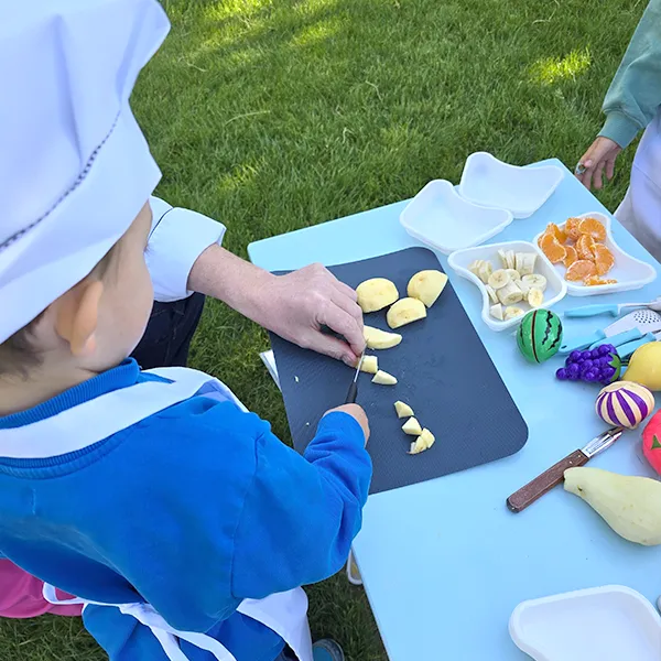 Enfants du groupe des Grands en pleine préparation de leur salade de fruits à la crèche 6 Sens, encadrés par un professionnel de Novae à Saint-Sulpice.