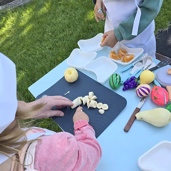 Enfants du groupe des Grands en pleine préparation de leur salade de fruits à la crèche 6 Sens, encadrés par un professionnel de Novae à Saint-Sulpice.